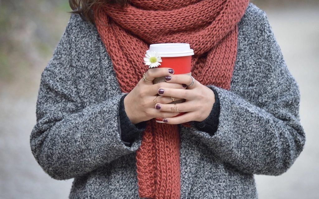Person in a grey wool coat and red knitted scarf holding a takeaway cup