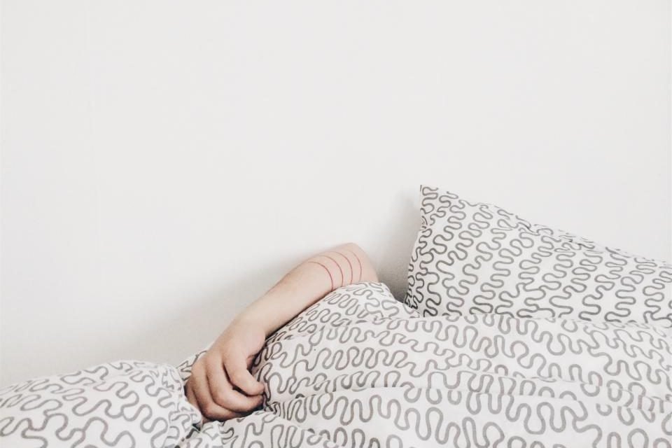 Arm resting on a patterned pillow on a white bed