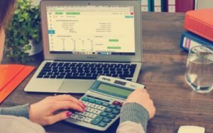 Hands using a calculator next to a laptop showing a spreadsheet