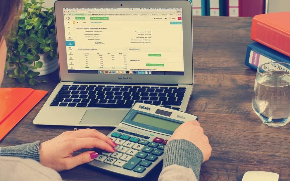 Hands using a calculator next to a laptop showing a spreadsheet