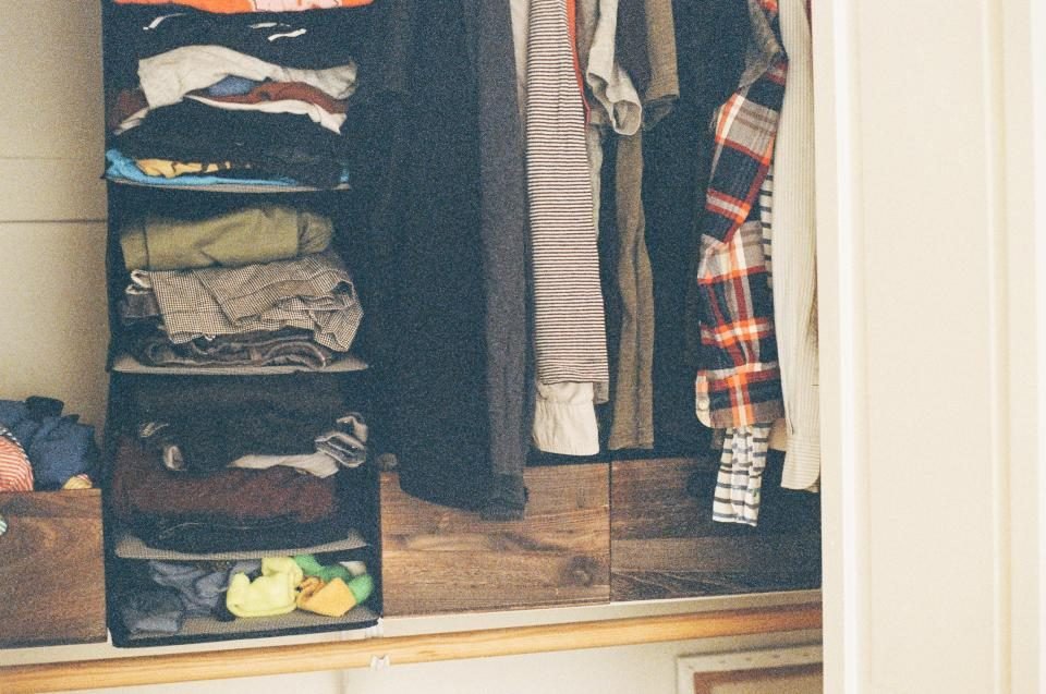 Open closet with folded clothes on shelves and shirts on hangers
