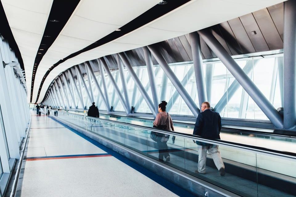 Travelers on a moving walkway in a bright airport terminal