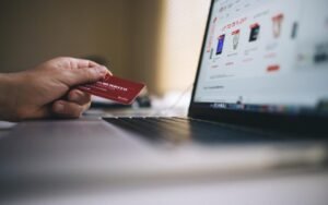 Hand holding a payment card in front of a laptop showing an online store