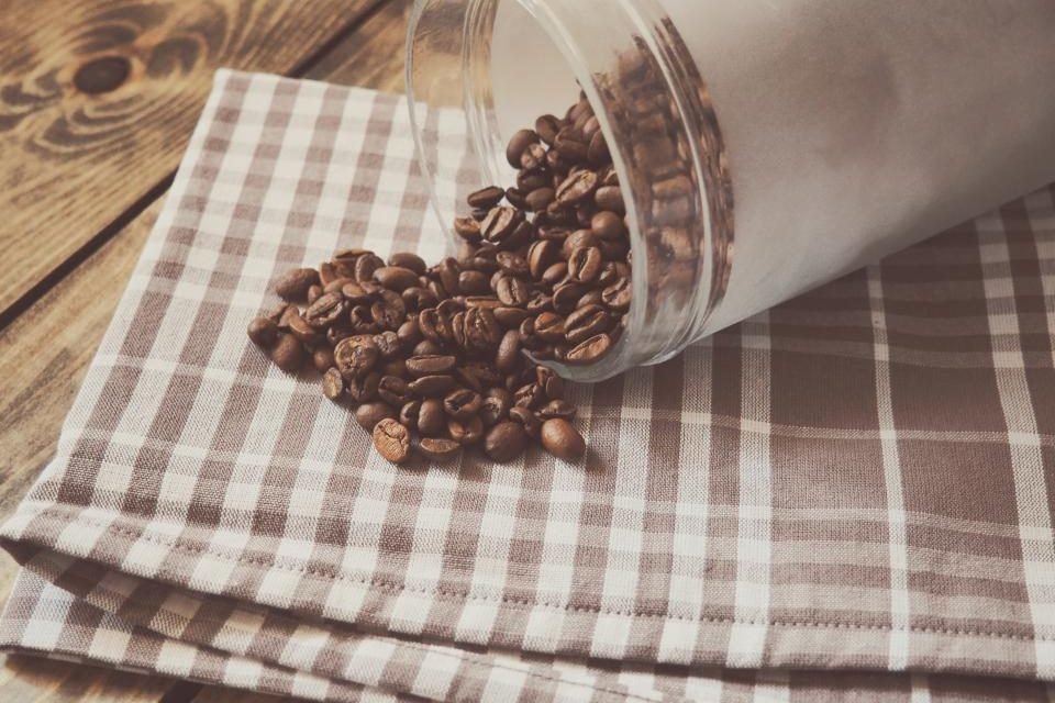 Coffee beans spilling from a glass jar onto a checked cloth