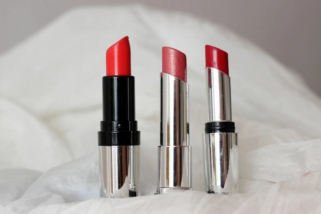 Three red lipsticks standing on a white cloth