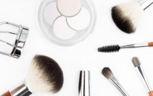 Makeup brushes, eyeshadow, mascara and an eyelash curler laid out on white