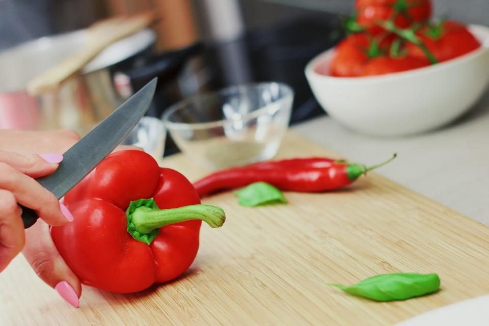 Hands slicing a red pepper on a wooden chopping board