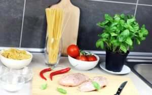 Kitchen counter with pasta, basil, tomatoes and chicken ready to cook