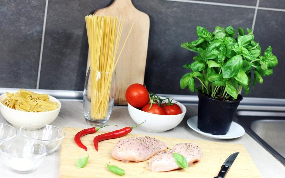 Kitchen counter with pasta, basil, tomatoes and chicken ready to cook