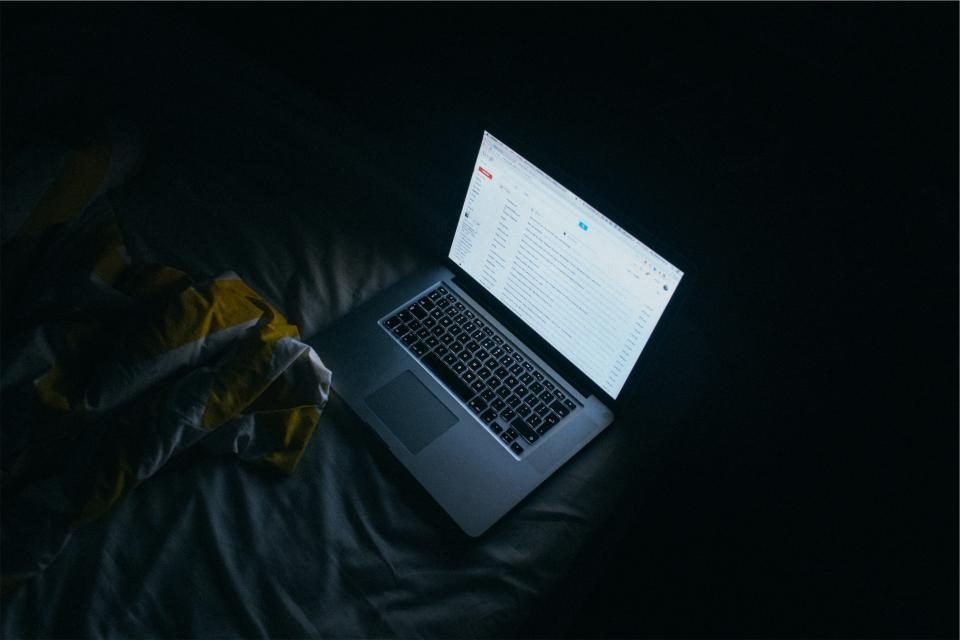 Laptop showing an email inbox on a bed in a dark room