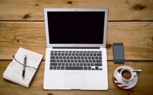 Laptop, notebook, phone and coffee cup on a wooden desk