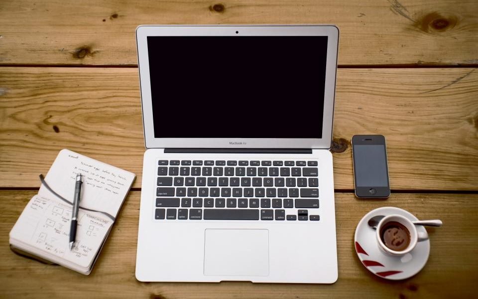 Laptop, notebook, phone and coffee cup on a wooden desk