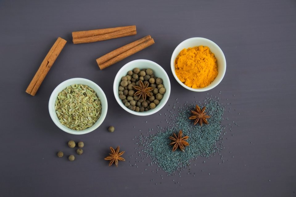 Small bowls of ground spices with cinnamon sticks and star anise