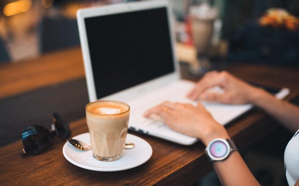 Hands typing on a laptop beside a cup of coffee