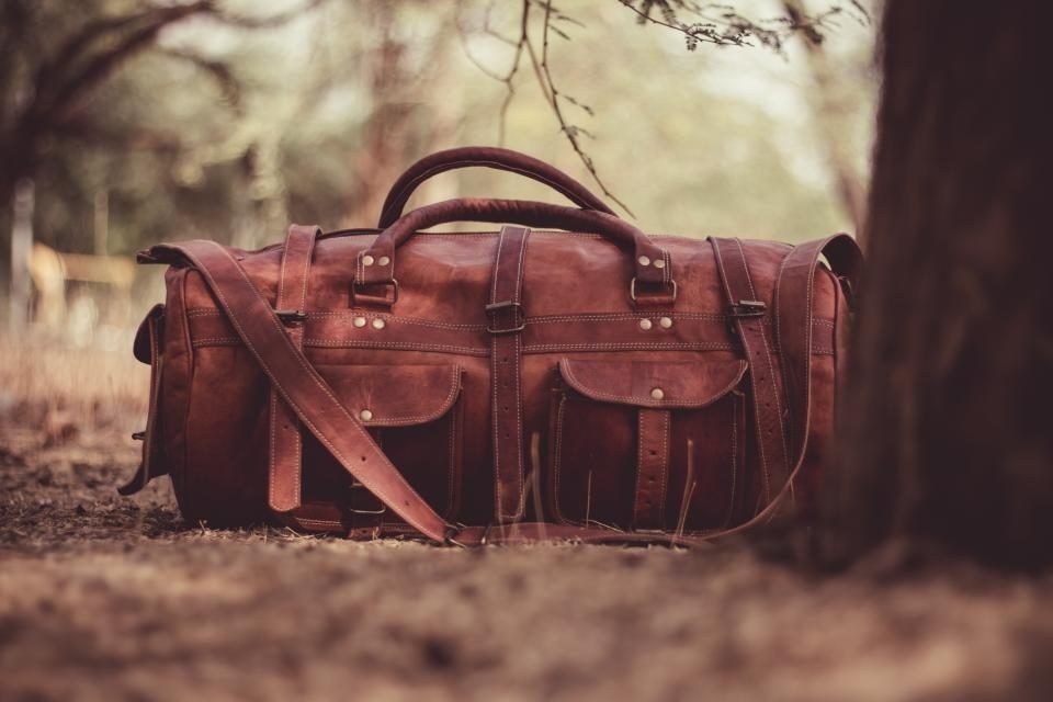 Brown leather duffel bag on the ground among trees