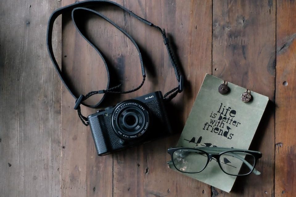 Compact camera, notebook and glasses on a wooden table
