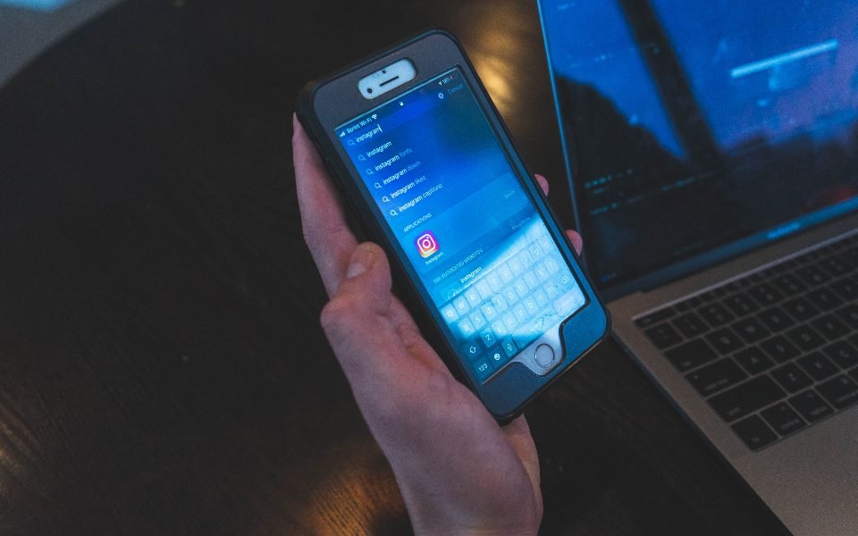 Hand holding a smartphone in front of a laptop