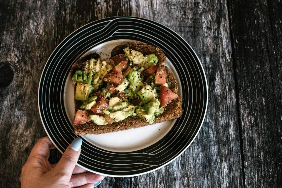 Open toast topped with avocado and tomato on a dark plate